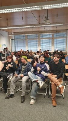 Eine Gruppe junger Menschen sitzt in einem Raum mit Stühlen und unterhält sich fröhlich miteinander.
