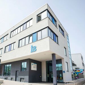Moderne Außenansicht eines weißen Gebäudes mit großen Fenstern und einem "IB"-Logo an der Fassade.