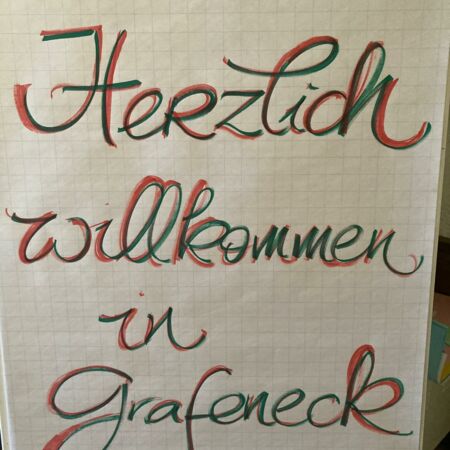 Ein handgeschriebenes Plakat mit der Begrüßung "Herzlich willkommen in Grafeneck" in roter und grüner Schrift.