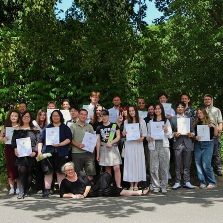 Gruppenfoto von Absolventen mit Urkunden vor einer grünen Kulisse, lächelnd und stolz. | © Name