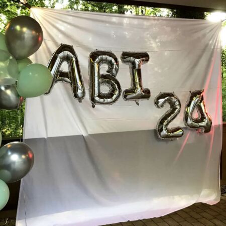 Silberne Luftballons formen die Aufschrift "ABI 24" vor einem weißen Hintergrund bei einer Feier.