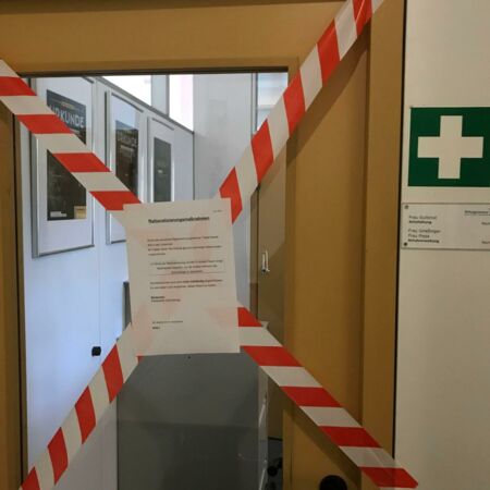 Ein Büro ist mit rot-weißem Absperrband und einem Schild zu Rationalisierungsmaßnahmen abgesperrt.