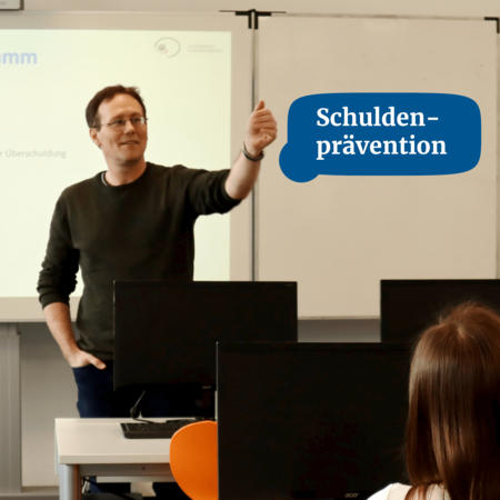 Ein Mann hält einen Vortrag über Schuldenprävention vor einer Klasse mit Computern.