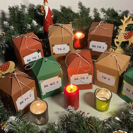 Weihnachtlich dekorierte Geschenkschachteln und Kerzen sind von Tannenzweigen und Rentierfiguren umgeben.