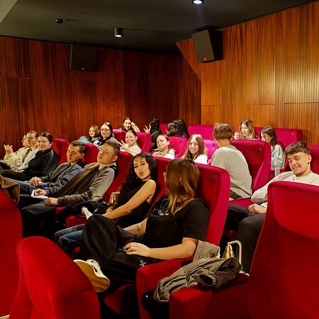 Eine Gruppe junger Leute sitzt in roten Kinosesseln und wartet gespannt auf den Film. | © CinemaLatino