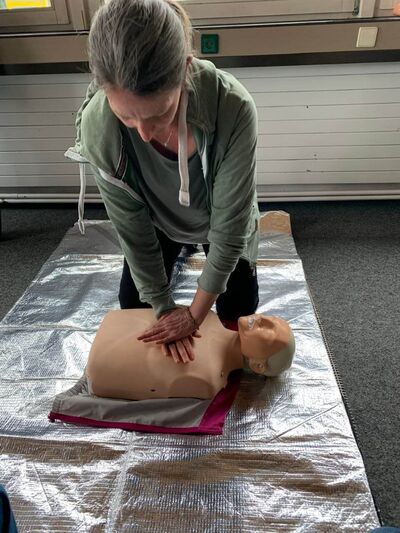 Eine Frau übt Erste-Hilfe-Maßnahmen an einer Puppe auf einer Rettungsdecke während eines PädTag-Workshops.