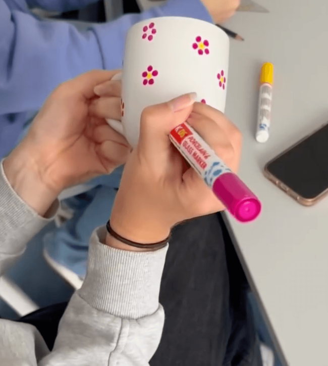 Ein Schüler gestaltet eine weiße Tasse mit bunten Blumenmotiven und einem Markierungsstift während eines Projekttags.