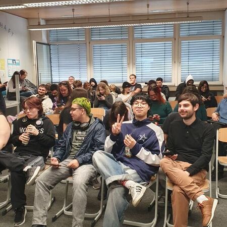 Eine Gruppe junger Menschen sitzt in einem Raum mit Stühlen und unterhält sich fröhlich miteinander.