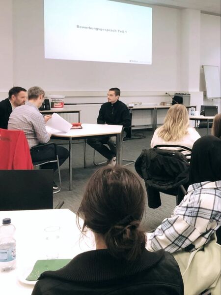 Teilnehmer eines Bewerbertrainings führen ein Vorstellungsgespräch in einem Schulungsraum durch. | © Brillux