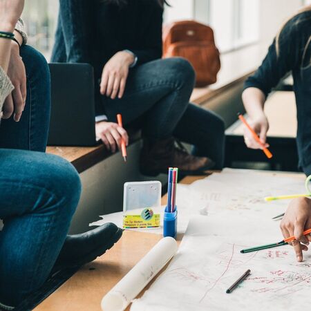 Eine Gruppe von Menschen arbeitet gemeinsam an einem Projekt, umgeben von Papier und Stiften auf einem Tisch.