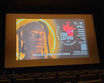 Ein Filmplakat für das CineLatino 2025 Festival wird auf einer Kinoleinwand präsentiert, mit leeren Sitzen im Vordergrund.