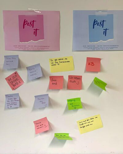 Bunte Post-it-Notizen mit Abschiedsbotschaften hängen an einer Wand während einer Abschlusszeremonie.