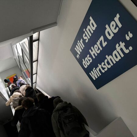 Menschen steigen eine Rolltreppe hinauf neben einem Schild mit der Aufschrift "Wir sind das Herz der Wirtschaft".