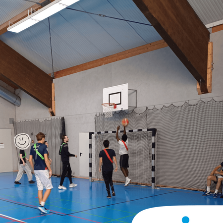 Schüler spielen Basketball in der Sporthalle einer Schule des IB, während einer einen Korb wirft.