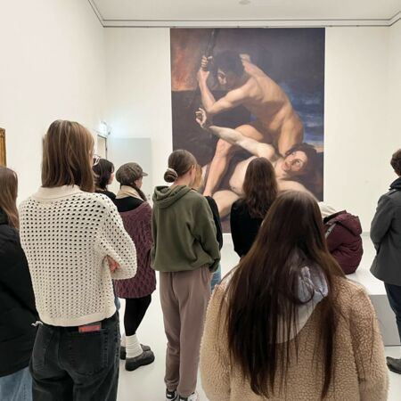 Eine Gruppe von Menschen betrachtet in einem Museum ein großes Gemälde, während eine Führung stattfindet.