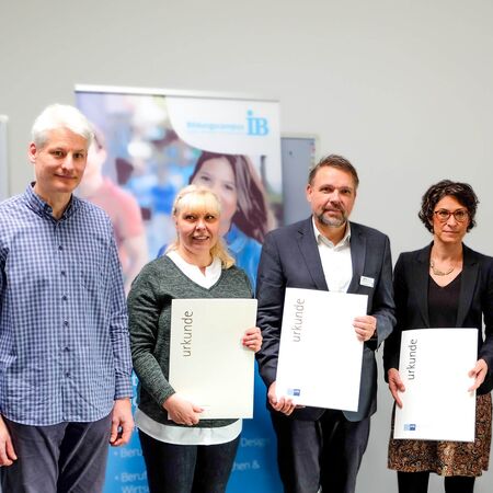 Vier Personen stehen nebeneinander, drei halten Zertifikate in den Händen und lächeln in die Kamera.
