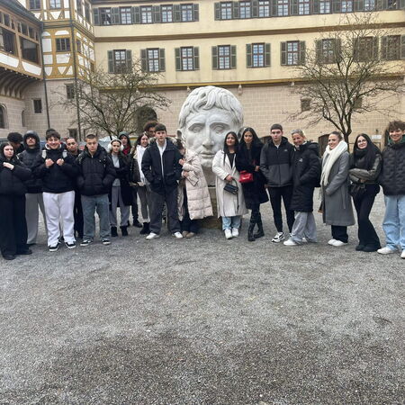 Eine Gruppe junger Menschen posiert vor einem großen Kopf-Skulptur auf einem historischen Innenhof.
