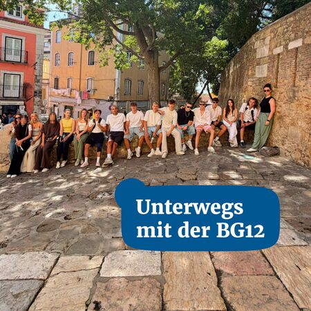 Schüler der BG12 genießen Zeit im Freien, sitzen an einer Steinstraße unter Bäumen in einer malerischen Stadt.
