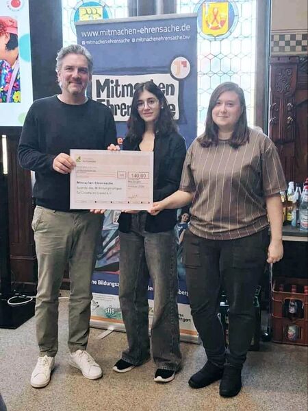 Drei Personen halten einen Scheck für die Initiative „Mitmachen Ehrensache“ bei einer feierlichen Veranstaltung.