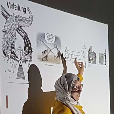 Eine Frau hält eine Präsentation vor einem Projektorbild mit dem Thema "Verteilung" und gestikuliert erklärend.