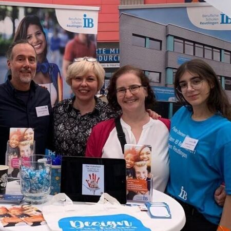 Vier Personen stehen lächelnd an einem Messestand mit Broschüren und Infomaterialien zum Thema Beruf und Bildung.