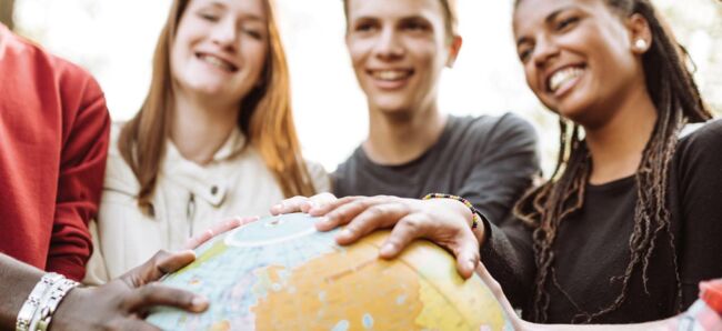 Vier Schüler:innen legen Ihre Hände auf einen Globus