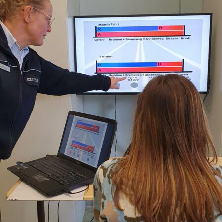 Eine Polizistin erklärt einer Frau an einem Bildschirm mit Diagrammen Verkehrssicherheitskonzepte.