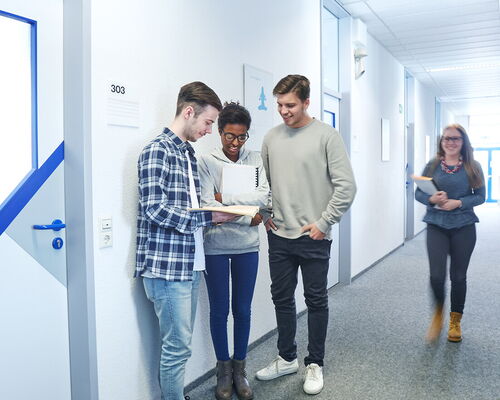 Vier Personen stehen in einem hellen Flur in Ulm, diskutieren angeregt über Dokumente.