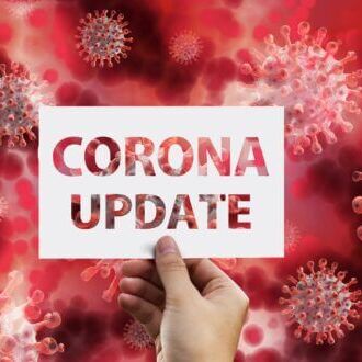Eine Hand hält ein Schild mit der Aufschrift "Corona Update" vor einem Hintergrund aus roten Virusabbildungen.