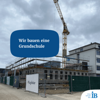 Eine Grundschule wird auf einer Baustelle mit Baukran und Gerüsten errichtet, begleitet von einem Werbeschild.