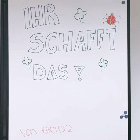 Eine Tafel zeigt die motivierende Botschaft "Ihr schafft das!" mit Klee und einem Marienkäfer verziert.