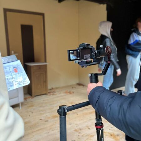 Eine Person filmt in einem Raum mit einem Stabilisator, während andere im Hintergrund vorbeigehen.