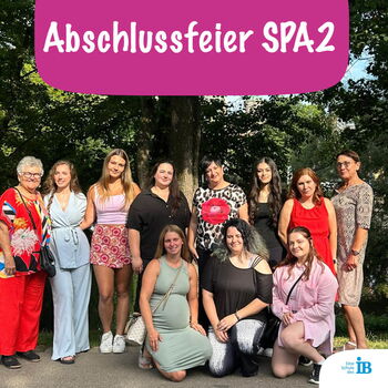 Eine Gruppe von Frauen posiert bei einer Abschlussfeier im Freien vor Bäumen mit einem Schild "Abschlussfeier SPA2".