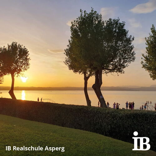 Menschen genießen den Sonnenuntergang am See während der Abschlussfahrt der 10. Klasse, umgeben von Bäumen.