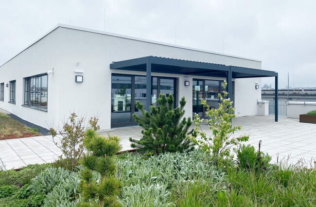 Moderne Dachterrasse eines Neubaus mit Pflanzen und Überdachung im Vordergrund, ideal für Entspannung.