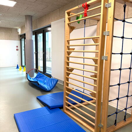 In einer Grundschule steht eine Sprossenwand mit blauen Matten und einem Parcours aus bunten Kegeln bereit.
