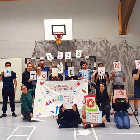 Eine Gruppe von Menschen hält ein Banner und Schilder mit dem Wort "Toleranz" und der Jahreszahl 2022 in einer Sporthalle.