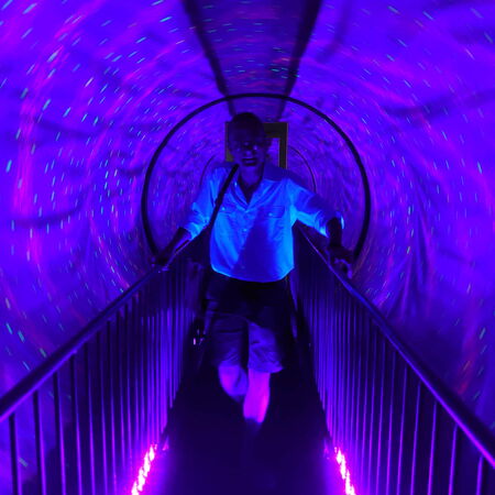 Eine Person geht durch einen leuchtenden, violetten Tunnel mit bunten Lichtpunkten, die eine futuristische Atmosphäre schaffen.