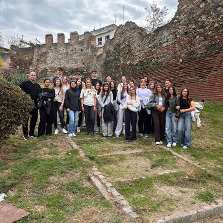 Eine Gruppe von Menschen posiert vor einer antiken Mauer in Thessaloniki unter bewölktem Himmel.