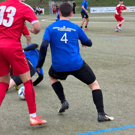 Ein Fußballspieler in blauer Trikots kämpft um den Ball, während ein Gegner in Rot ihn herausfordert.