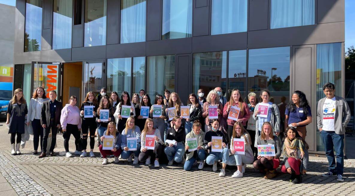 Eine Gruppe von Menschen posiert vor einem Gebäude und hält bunte Schilder bei der Netzwerkkonferenz 2021.