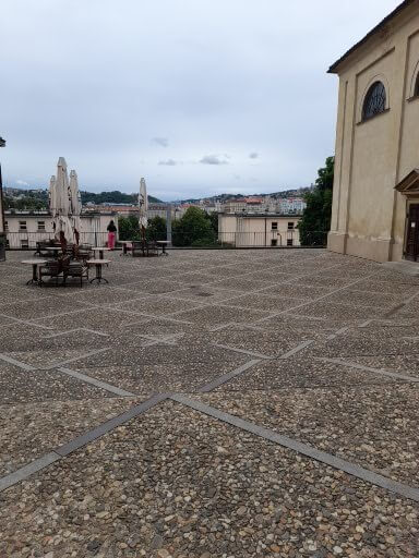 Ein ruhiger Platz mit Tischen, Stühlen und Blick auf die Landschaft hinter einem historischen Gebäude.