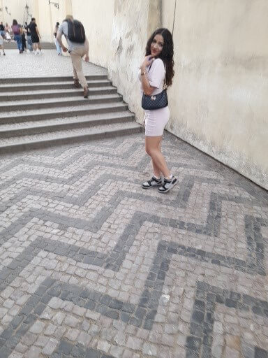 Eine Frau in einem rosa Outfit posiert auf einem gestreiften Pflaster vor einer Treppe.