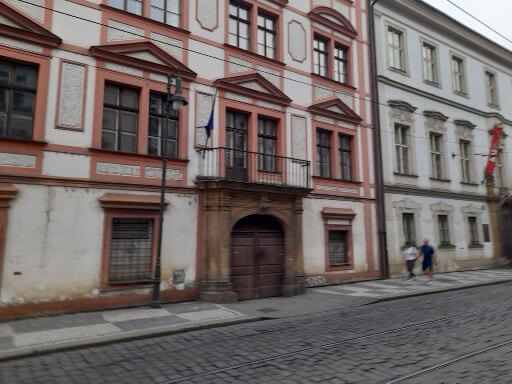 Stadtszene mit historischem Gebäude und Fußgängern auf einem gepflasterten Weg in einer ruhigen Straße.