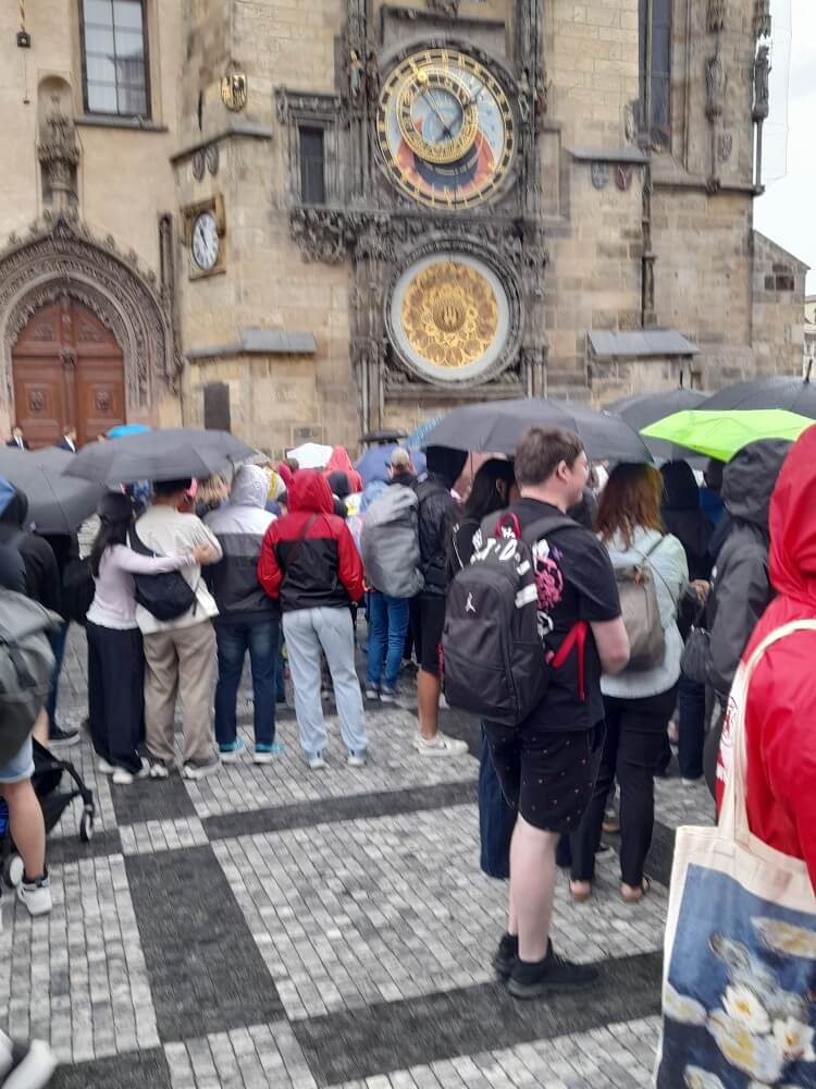 Menschen stehen unter Regenschirmen vor der astronomischen Uhr in Prag und warten auf das Uhrenspiel.