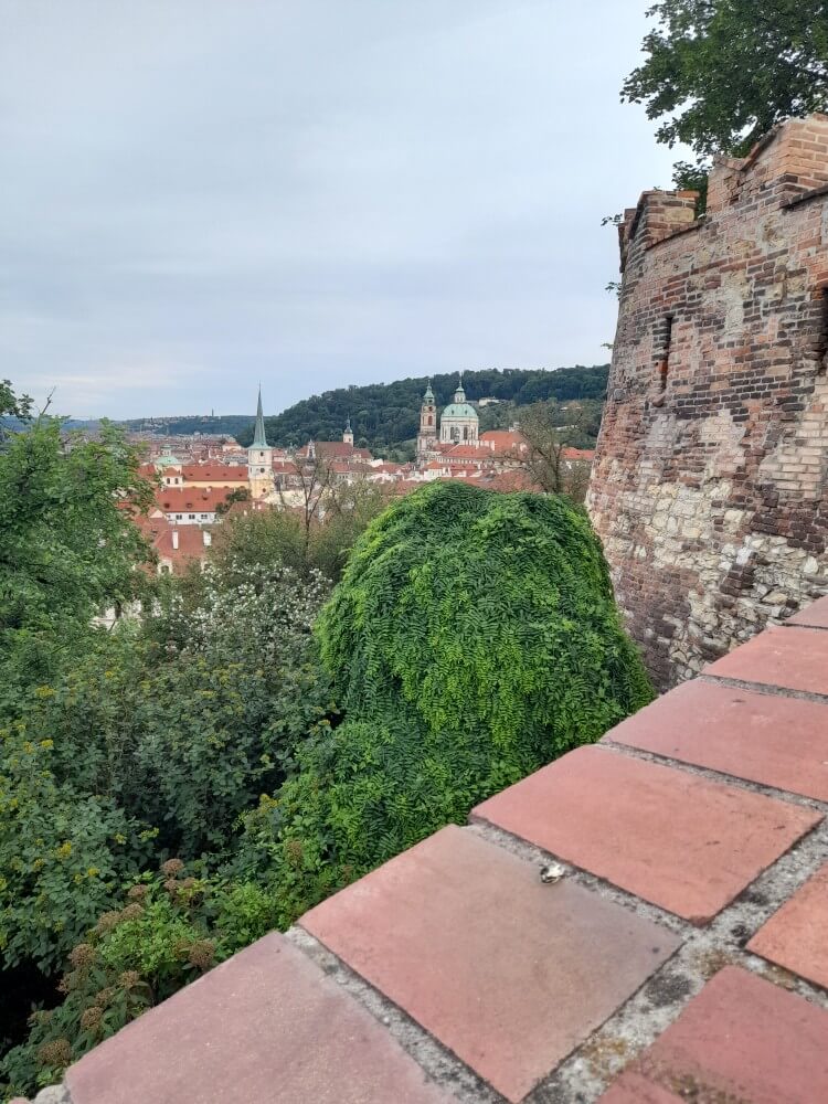 Blick auf die Stadt mit roten Dächern und einer alten Mauer, umgeben von üppigem Grün und sanften Hügeln.