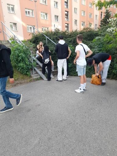 Eine Gruppe von Jugendlichen entspannt an einer Treppe vor Wohngebäuden in der Stadt und unterhält sich.