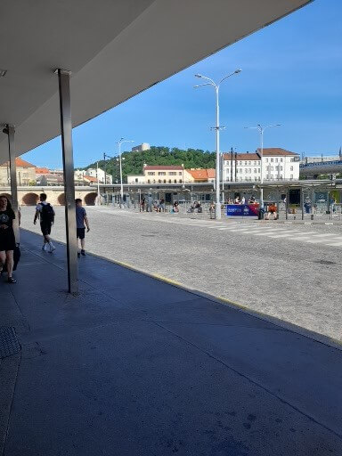 Eine breite Straße mit Passanten, blickend auf Gebäude und Hügel unter blauem Himmel.