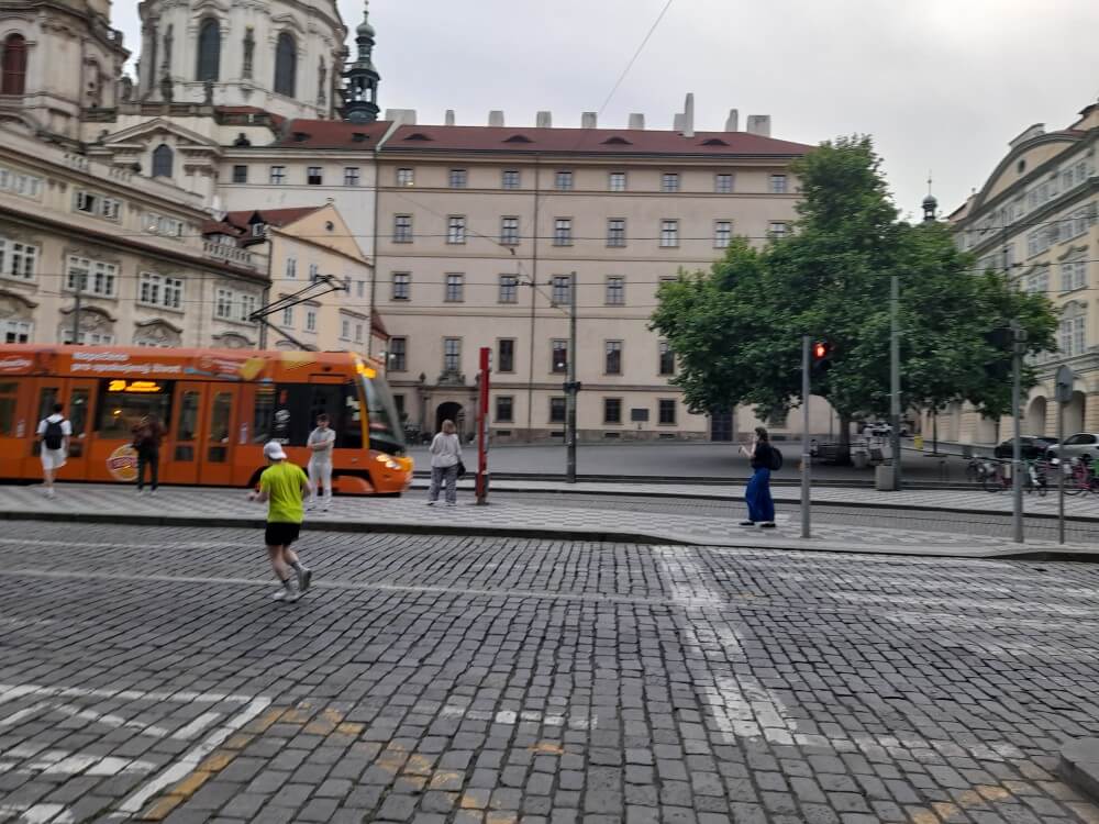 Ein orangefarbener Straßenbahnwagen fährt durch eine belebte Straße mit historischen Gebäuden im Hintergrund.