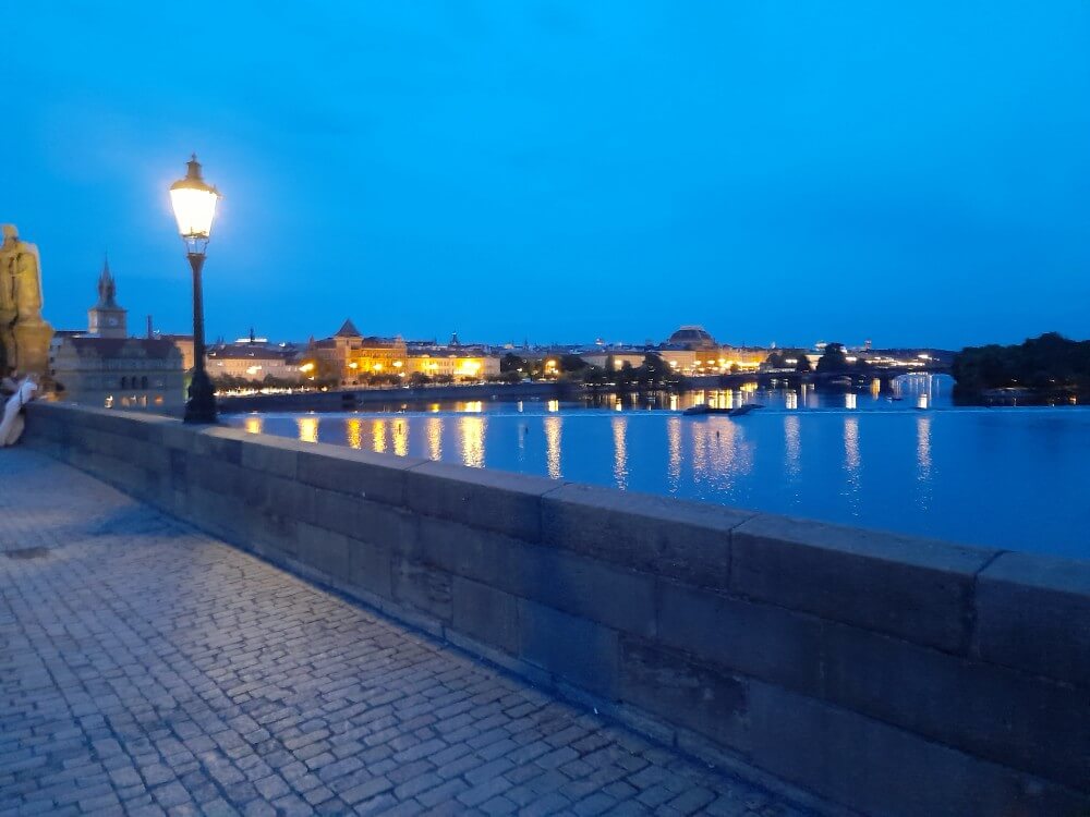 Die beleuchtete Uferpromenade spiegelt die Stadtlichter im Wasser bei Abenddämmerung wider.